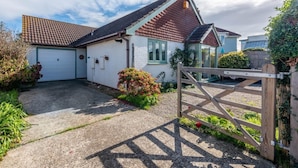 Einbungalow mit Garage, Holztor und kleinem Garten mit Blumen und Sträuchern.