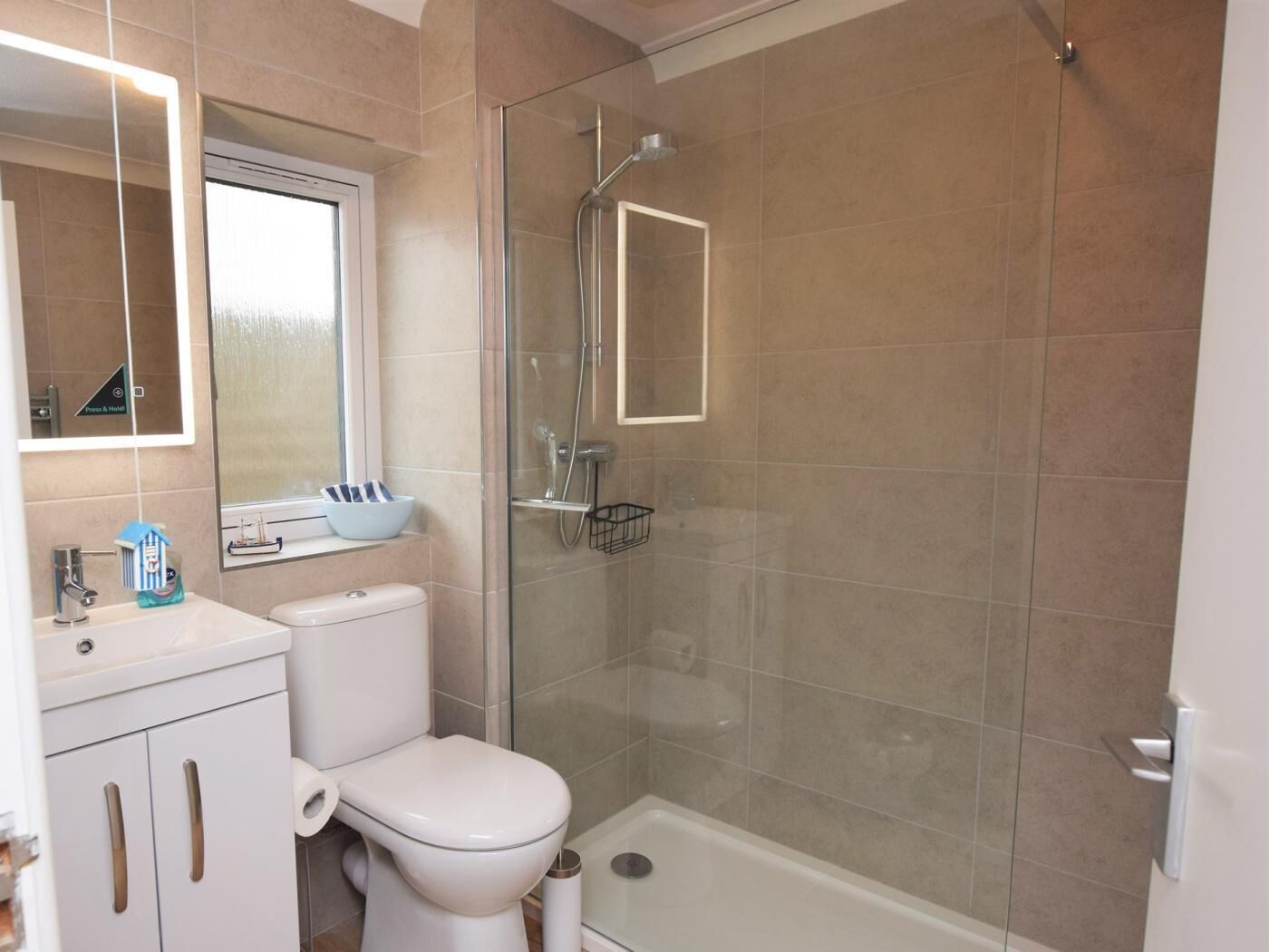 Une salle de bain comprenant des toilettes, une douche fermée par une paroi de verre et un lavabo avec un miroir.