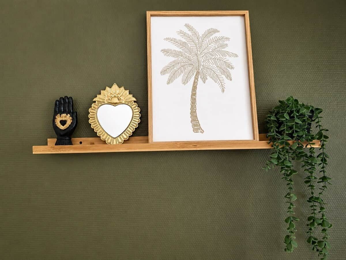 En inramad bild av ett palmträd, placerad på en hylla av trä mot en grön vägg.