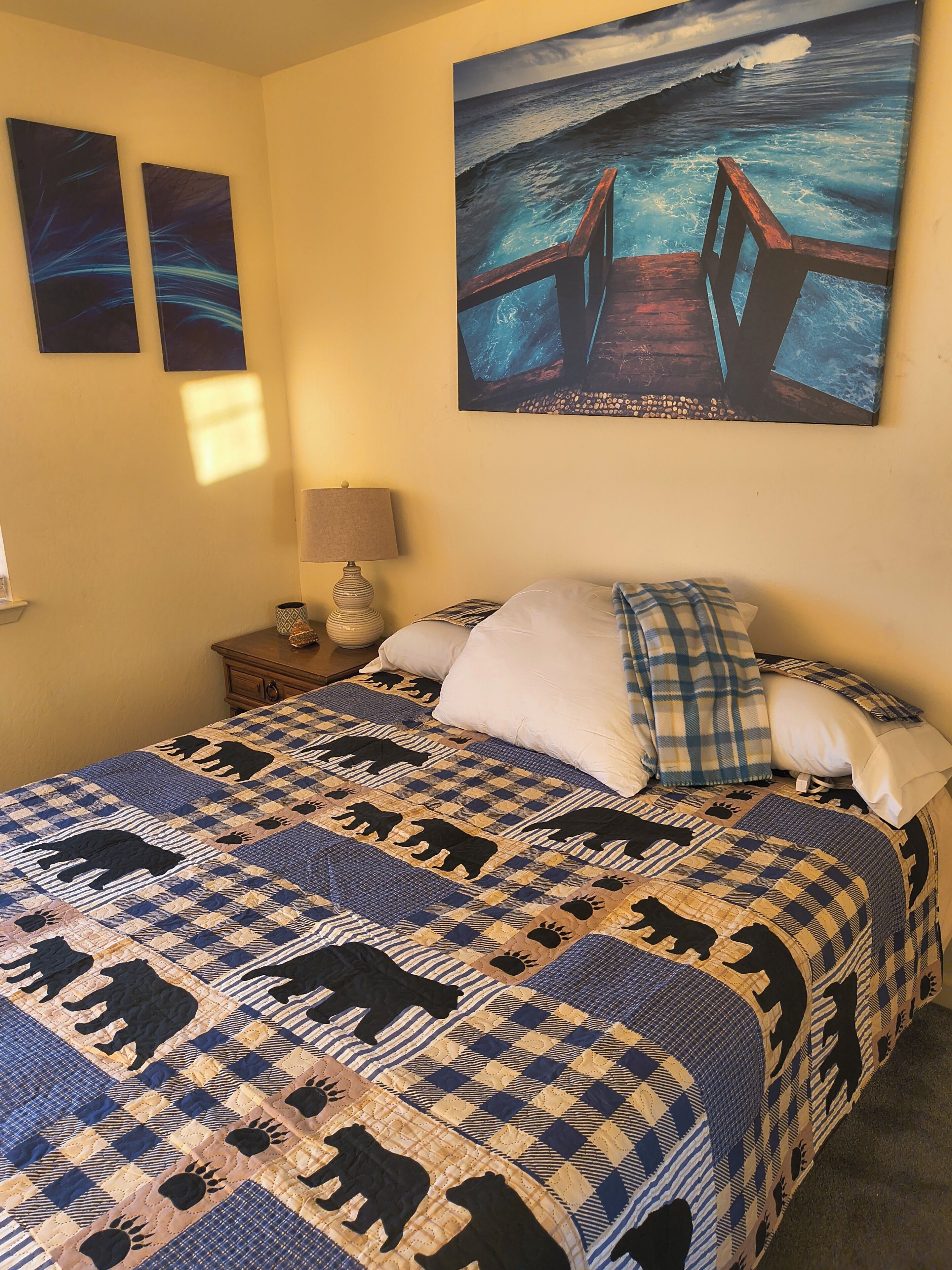 Une chambre à coucher avec un lit, une table de chevet, une lampe et un tableau représentant un pont au-dessus de l’eau.