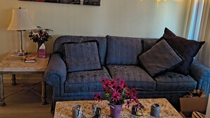 Ein Wohnzimmer mit einer Couch, einem Couchtisch mit Blumen, einer Lampe und einem Bild an der Wand.