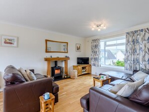 A living room with a fireplace, leather sofas, a television, and a window with curtains. - 3 Bed in Swanage (oc-79405) (Swanage)