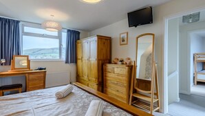 Une chambre à coucher comprenant un lit, une armoire en bois, une commode, un miroir, un bureau, une chaise et un téléviseur.