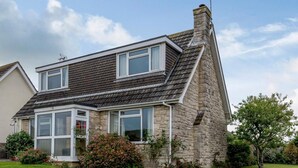 Une maison à deux étages avec une façade en pierre, de grandes fenêtres et une pelouse bien entretenue.