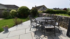 Une terrasse avec une table ronde et des chaises, entourée d’un mur de pierre et de verdure.