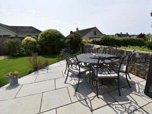 A patio with a round table and chairs, surrounded by a stone wall and greenery. - 3 Bed in Swanage (oc-79405) (Swanage)