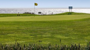 Ein Golfplatz mit Fahne, Hinweisschild und Blick auf den Ozean.