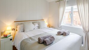 Ein ordentlich bezogenes Bett mit Kissen, einer Nachttischlampe und aufgerollten Handtüchern auf einer weißen Bettdecke.