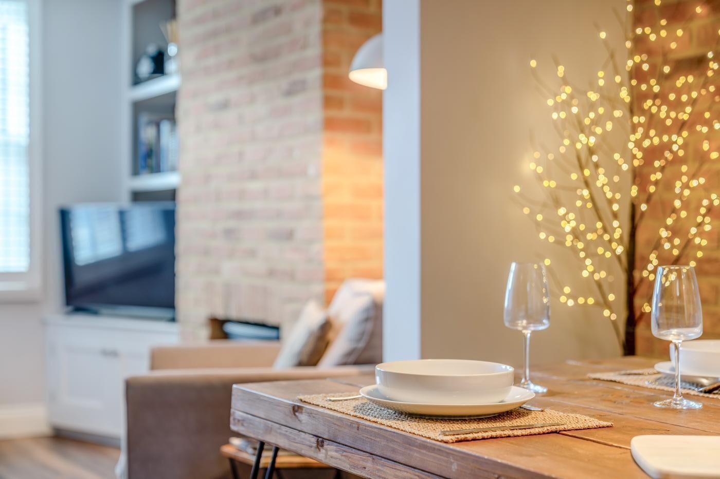 A dining table set with plates and glasses, a brick wall, and a television in the background.