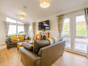 Ein modernes Wohnzimmer mit Ledersofas, einem Flachbildfernseher und großen Fenstern.