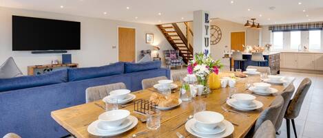 A modern living room with a large sofa, a dining table set for four, and a kitchen in the background.