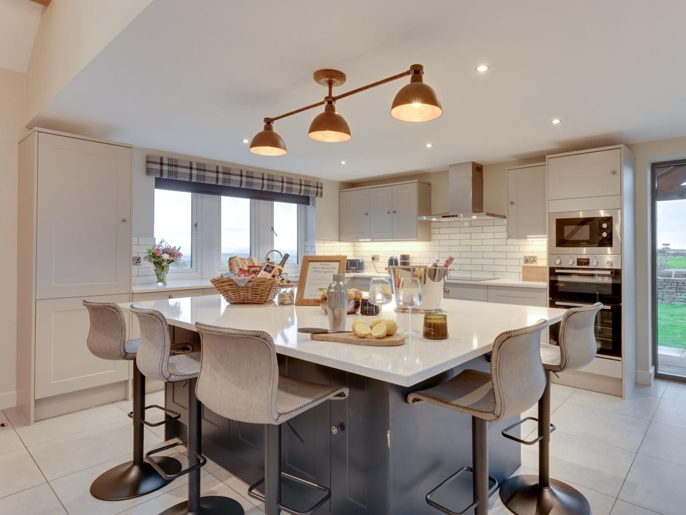 A modern kitchen with a central island, bar stools, and a view of the outdoors.
