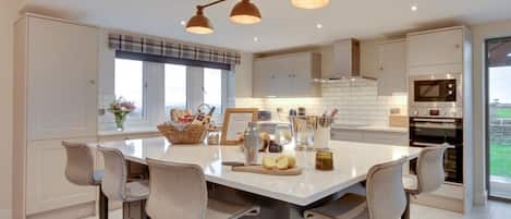 Una cocina moderna con una isla central, taburetes de bar y vistas al exterior.