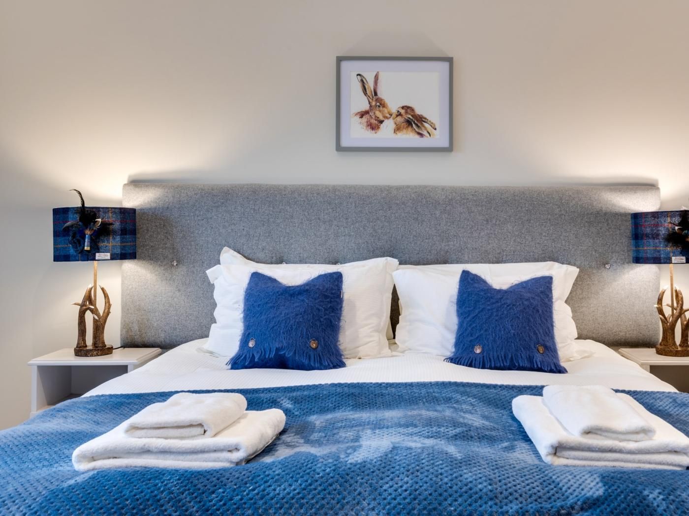 A neatly made bed with two pillows, a blue blanket, and two folded towels.