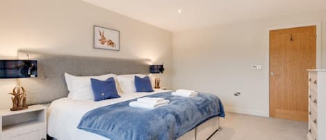 A bedroom with a bed, bedside tables, a nightstand, a wooden door, and a wall-mounted light fixture.