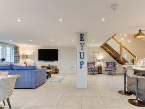 A spacious living room with a large flat-screen TV, a blue sofa, and a modern staircase. - 6 Bed in Scammonden (oc-79287) (Huddersfield)