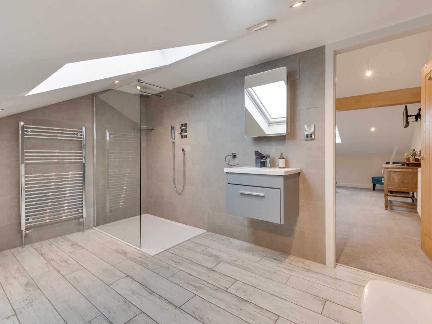 A modern bathroom with a glass shower enclosure, a vanity with a mirror, and a skylight above.