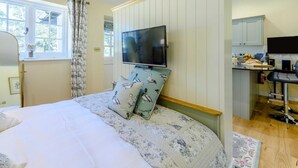 A bedroom with a bed, a TV mounted on the wall, a window with curtains, and a small kitchenette area. - 1 Bed in Lewes (oc-79182) (Beddingham)