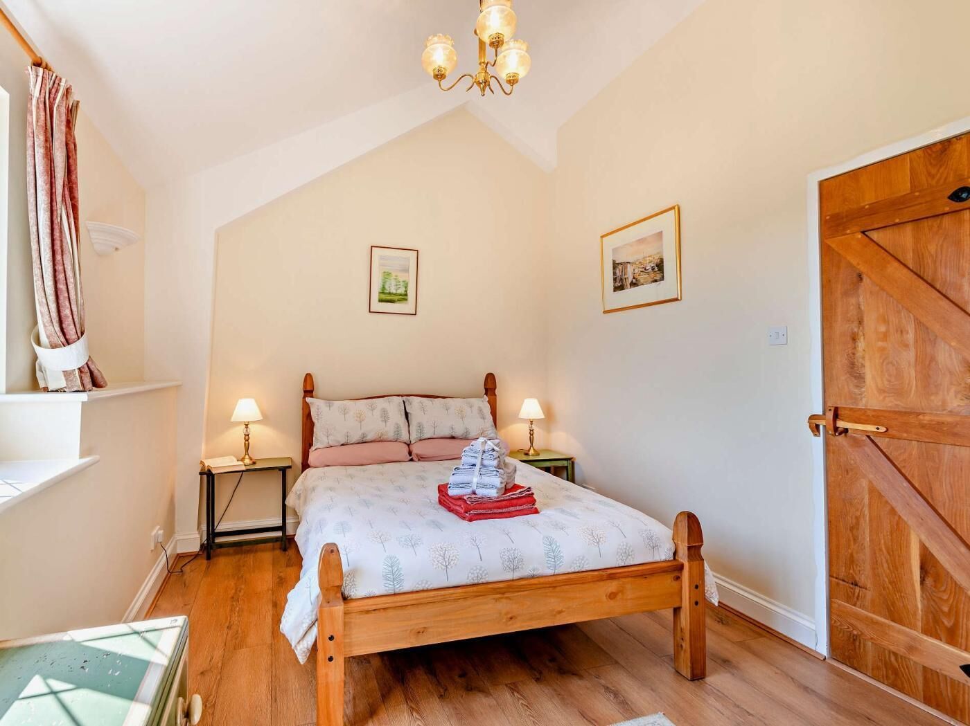 Une chambre à coucher avec un lit en bois, deux tables de chevet avec des lampes, un lustre et une grande porte en bois.