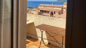 Ein Balkon mit Tisch und Stühlen, mit Blick auf eine Küstenlandschaft mit Gebäuden und blauem Himmel.