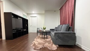 Ein Wohnzimmer mit grauem Sofa, Fernseher, einem flauschigen Teppich und einer Tür.