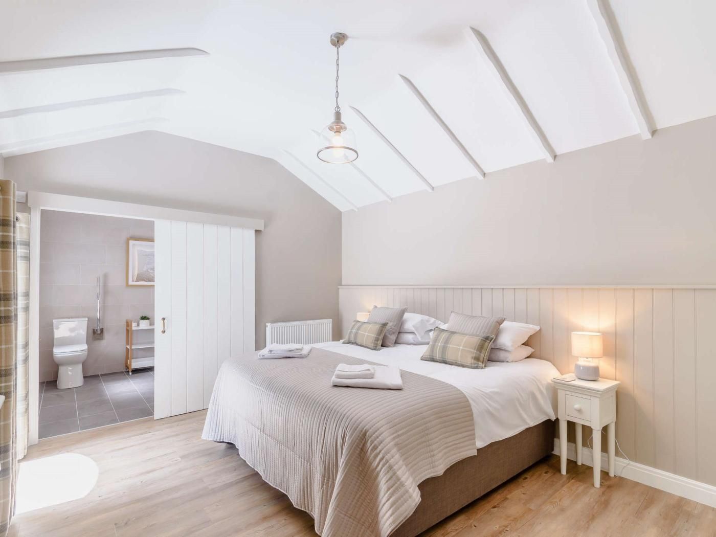Ein Schlafzimmer mit einem großen Bett, Nachttischen, einer Deckenleuchte und Blick ins Badezimmer.
