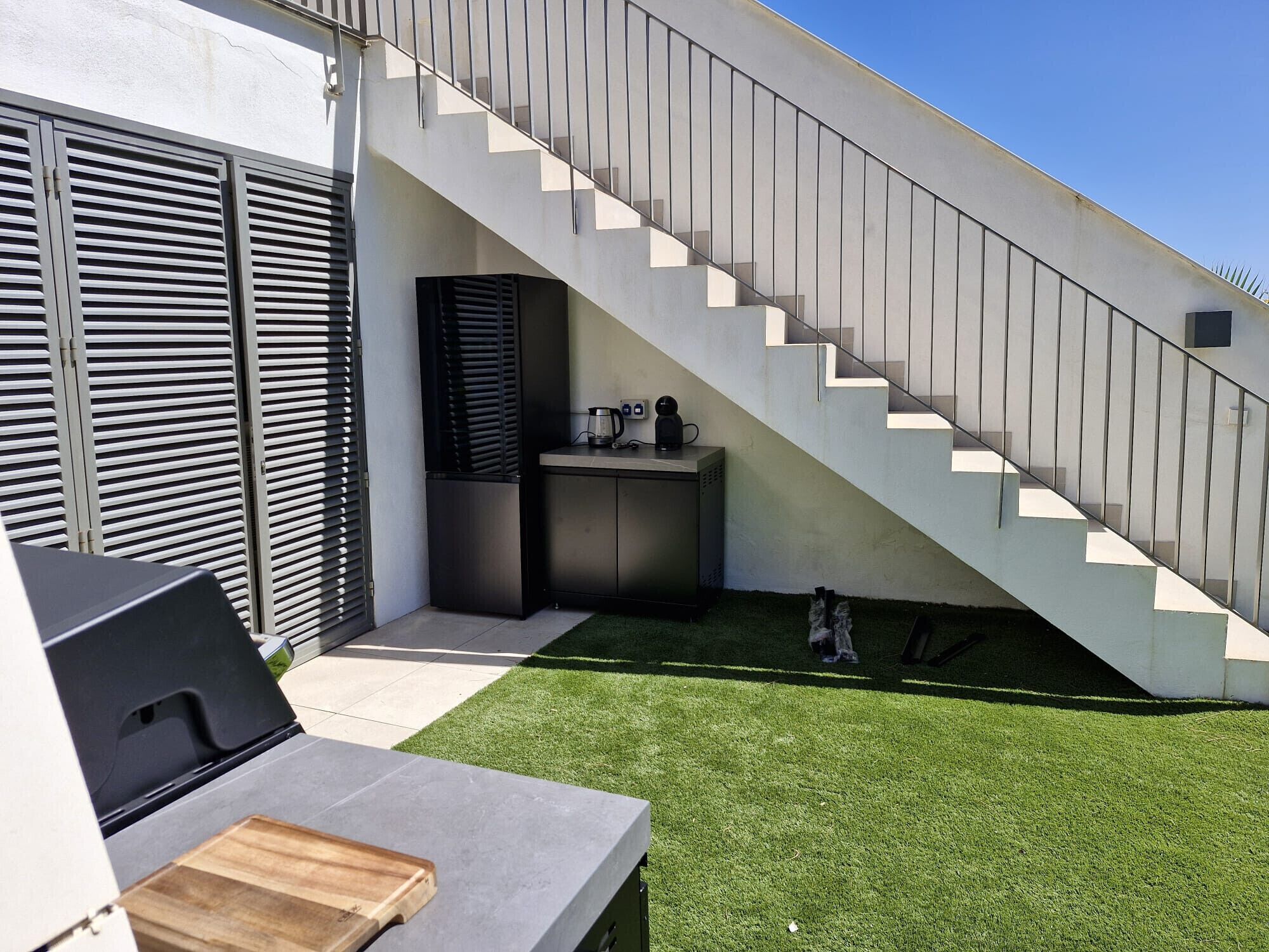 Un espace extérieur moderne comprenant un escalier, un barbecue et un petit meuble de rangement.