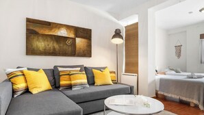 Una sala moderna con un sofá gris, almohadones amarillos, una mesa de centro redonda y un cuadro abstracto grande en la pared.