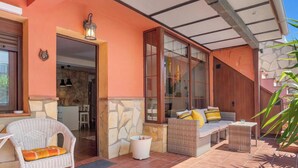 Un patio exterior con mobiliario de mimbre, un muro de piedra y un ventanal que da a un espacio interior.