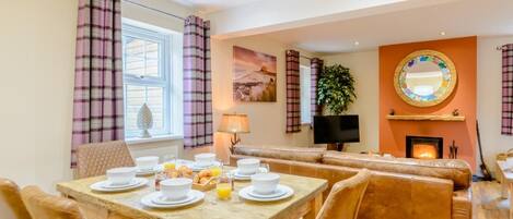 A dining area with a wooden table set for breakfast, a sofa, and a fireplace.