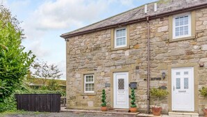 A stone building with two white doors, a small window, and a gravel driveway. - 3 Bed in Chathill (oc-79566) (Beadnell)