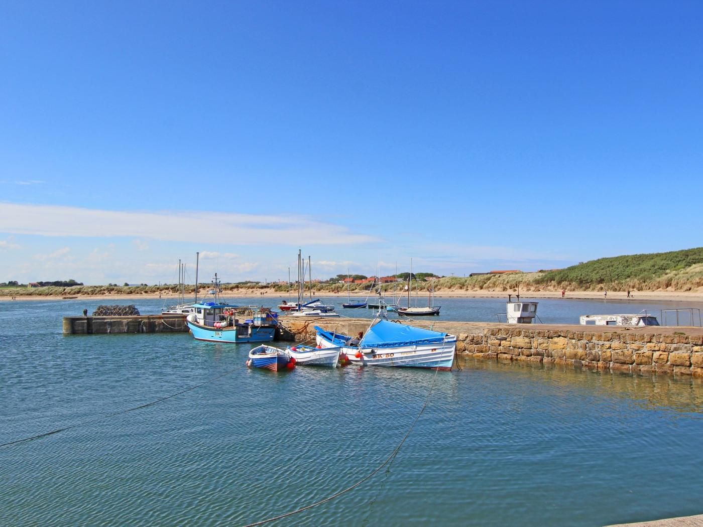 Ein ruhiger Hafen mit vertäuten Booten, einem steinernen Wellenbrecher und blauem Himmel.