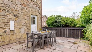 A stone building with a door and window, a patio with a table and chairs, and a wooden fence. - 3 Bed in Chathill (oc-79566) (Beadnell)
