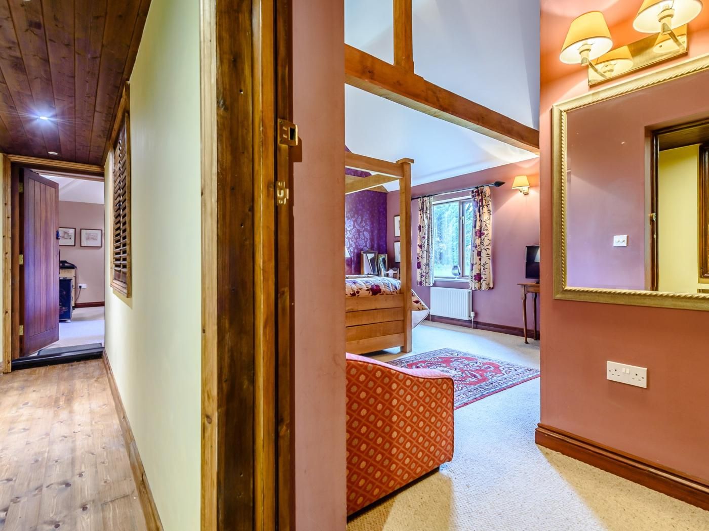 A hallway leading to a bedroom with a bed, a window with curtains, and a lamp.