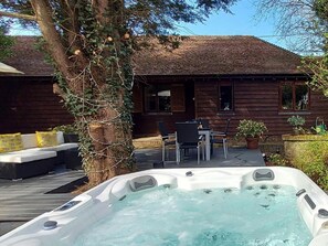 Ein Holzhaus mit Whirlpool, Sitzgelegenheit im Freien und einem Baum.