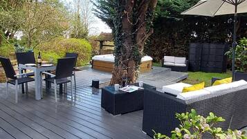 An outdoor deck with a dining table, chairs, a hot tub, and a sofa with cushions.