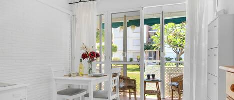 Ein Zimmer mit Esstisch und Stühlen, ein kleiner Tisch mit Blumenvase und Blick auf eine Wohngegend durch eine Glastür.