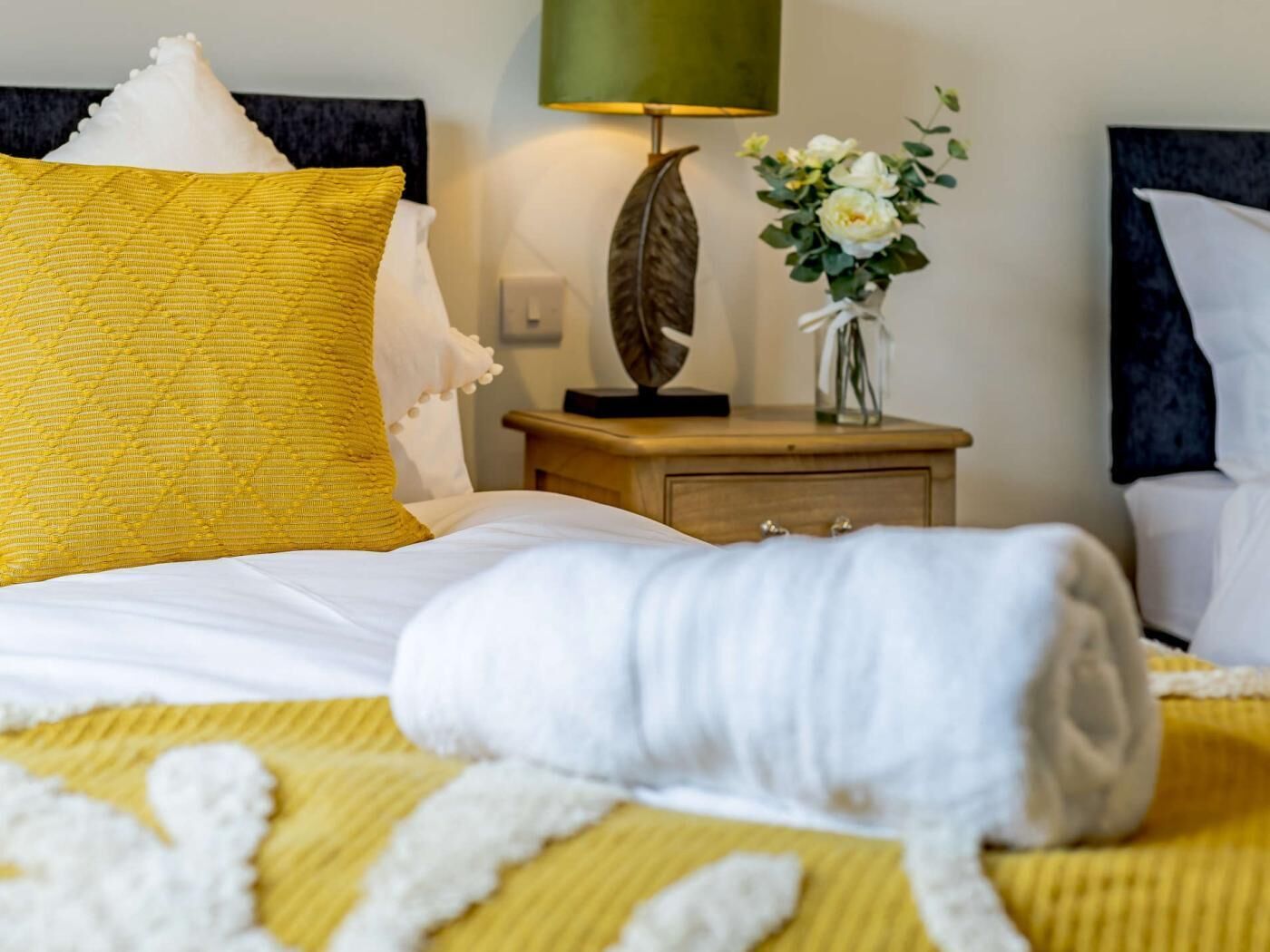 Un lit bien fait, avec une couette jaune, un oreiller blanc et une serviette blanche enroulée.