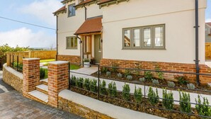 A two-story house with a brick facade, a front porch, and a garden with a metal fence. - 2 Bed in Newton Tracey (oc-80381) (Newton Tracey)