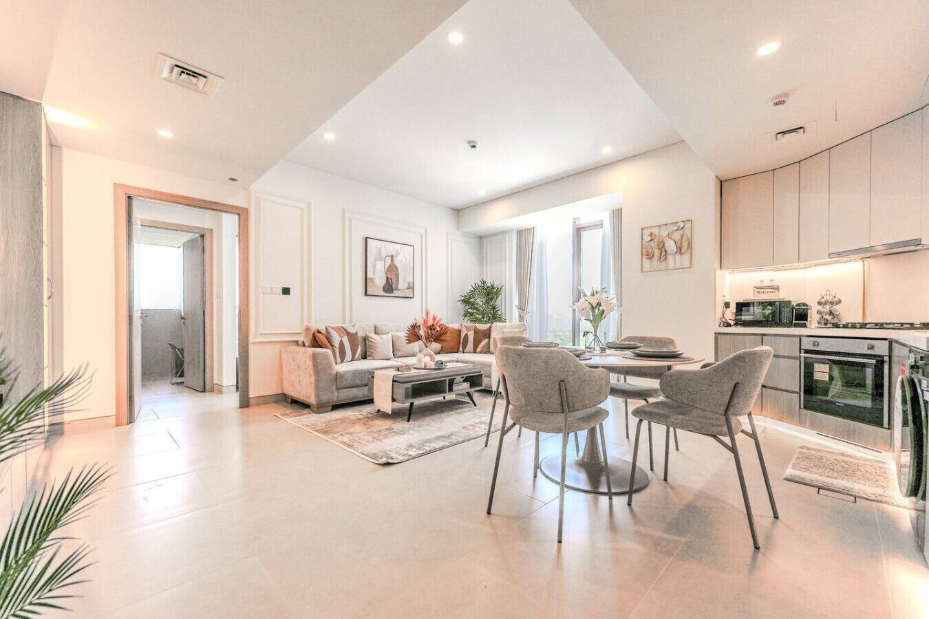 Un vaste espace de vie comprenant un canapé, une table à manger et des chaises, une cuisine équipée d’appareils modernes, et un couloir menant à une autre pièce.