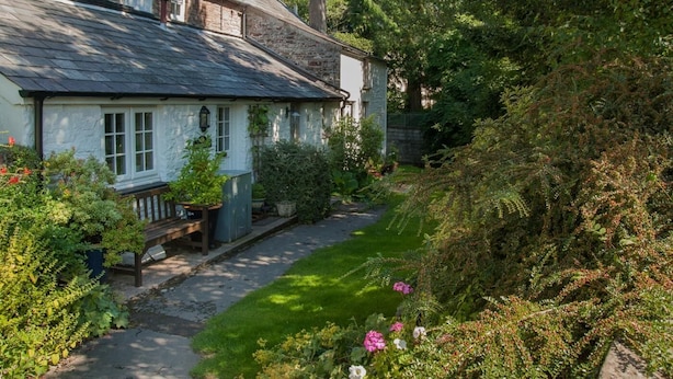 A traditional stone house with a sloped roof, a stone chimney, and a small garden with a pathway leading to the entrance. - 2 Bed in Brecon (oc-bn016) (Talybont-on-Usk)