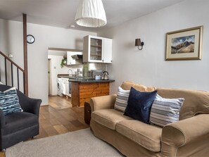 A living room with a sofa and armchair, a kitchen area with cabinets and a sink, and a staircase. - 2 Bed in Brecon (oc-bn016) (Talybont-on-Usk)