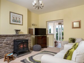 Una sala de estar con chimenea de piedra, televisor, sofá y vistas a través de un ventanal.