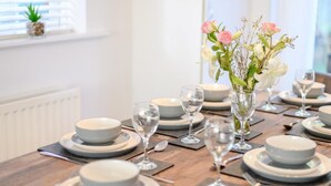 A dining table set with plates, glasses, and a vase of flowers. - 4 Bed in Brockenhurst (oc-80420) (Brockenhurst)