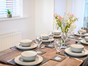 A dining table set with plates, glasses, and a vase of flowers. - 4 Bed in Brockenhurst (oc-80420) (Brockenhurst)