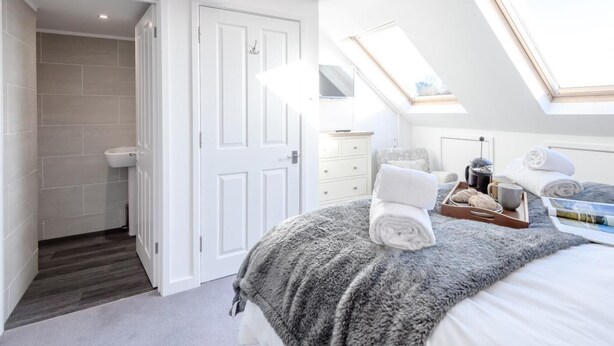 A bedroom with a skylight, a bed with a grey blanket, a bedside table with a kettle, and a small window. - 4 Bed in Brockenhurst (oc-80420) (Brockenhurst)
