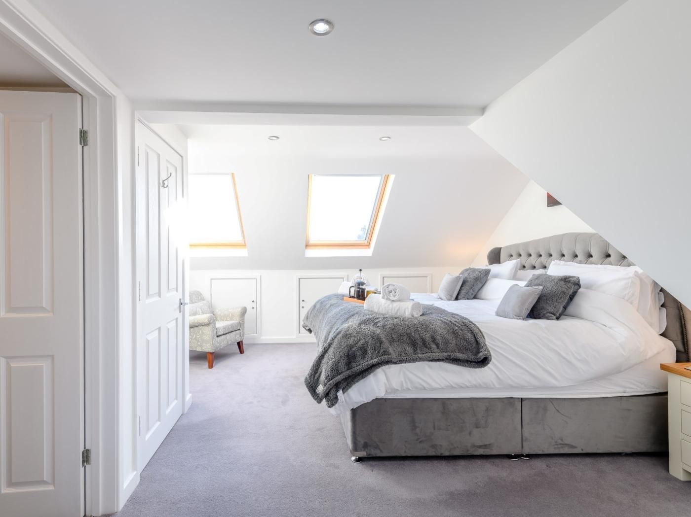 Een slaapkamer met een groot bed, een stoel, een nachtkastje en een dakvenster.