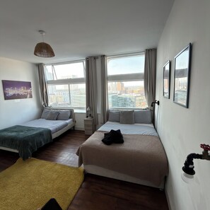 A hotel room with two beds, a view of the city, and a cityscape painting on the wall. - Manchester City Centre/ Prime Location Apartment (Salford)