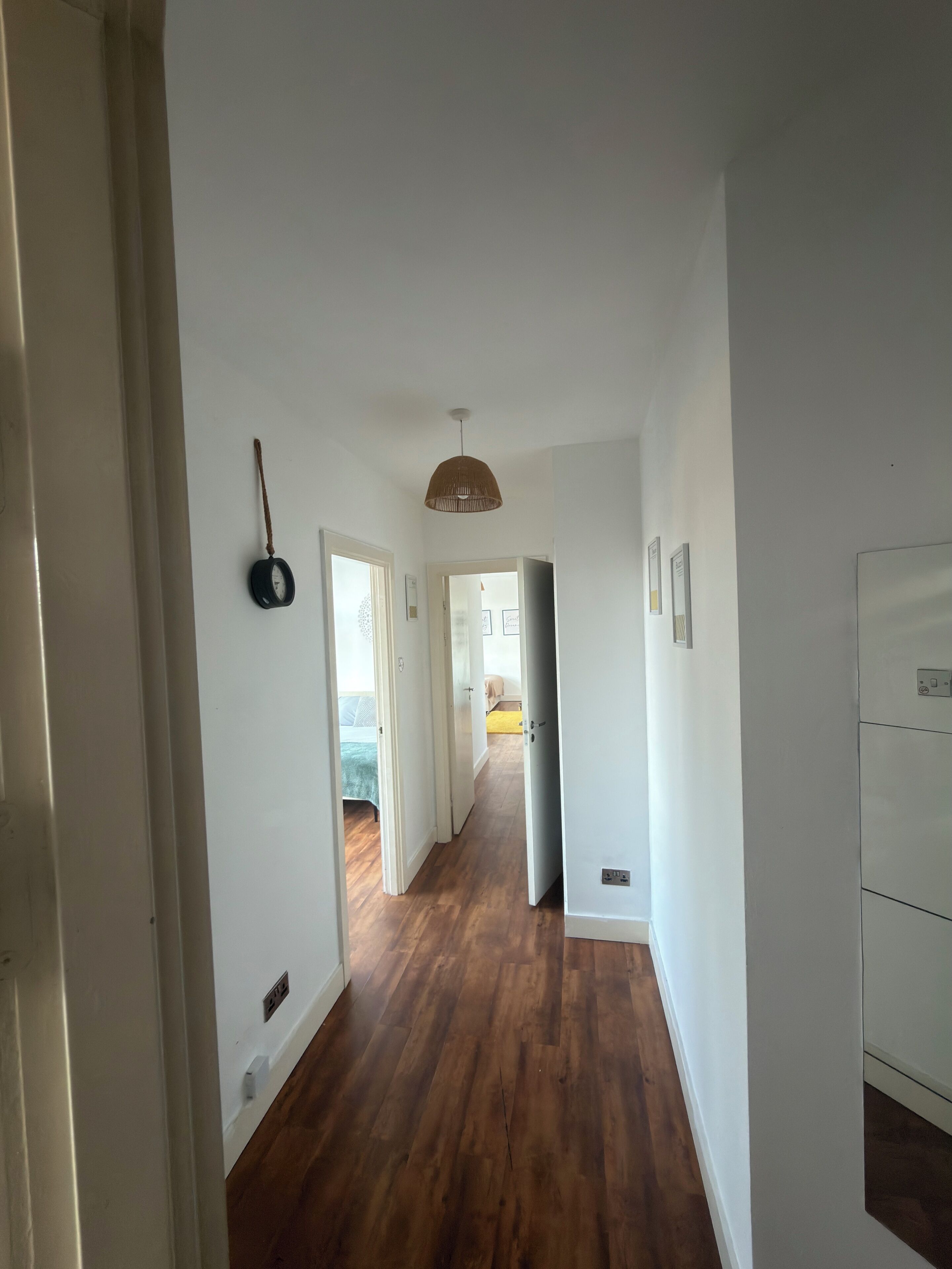 Un couloir doté d’un plancher en bois, de murs blancs et d’un luminaire suspendu.