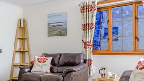 A brown leather sofa, a wooden ladder, a painting, a window with curtains, and a small wooden table with a teapot.